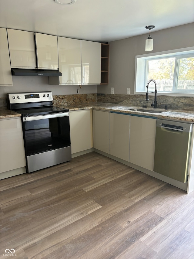 kitchen featuring sink, stainless steel appliances, light hardwood / wood-style flooring, and dark stone counters