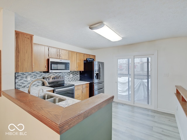 kitchen with stainless steel appliances, kitchen peninsula, sink, backsplash, and light hardwood / wood-style flooring