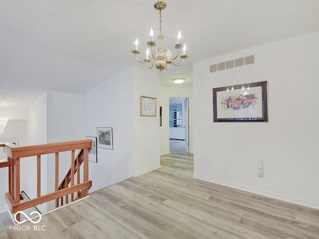 interior space with light wood-type flooring, a textured ceiling, and an inviting chandelier