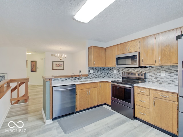 kitchen featuring stainless steel appliances, pendant lighting, sink, a chandelier, and light hardwood / wood-style flooring