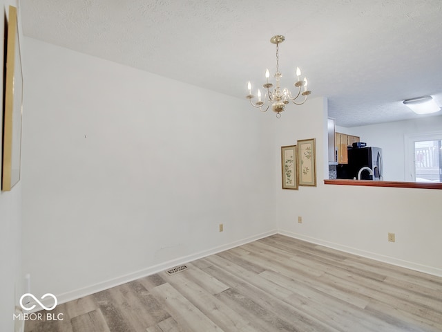 spare room featuring a chandelier, a textured ceiling, and light hardwood / wood-style flooring