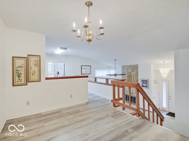 interior space featuring ceiling fan with notable chandelier, a textured ceiling, light wood-type flooring, and vaulted ceiling