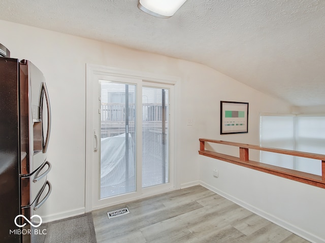 interior space featuring lofted ceiling, a textured ceiling, and light hardwood / wood-style flooring