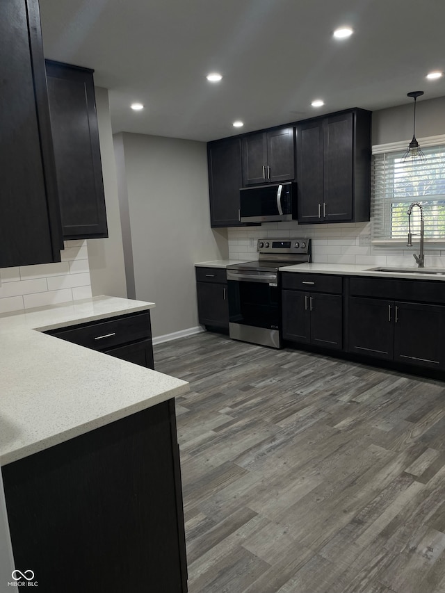 kitchen with appliances with stainless steel finishes, backsplash, decorative light fixtures, light wood-type flooring, and sink