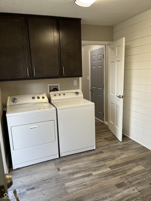 washroom featuring wood walls, hardwood / wood-style floors, separate washer and dryer, a textured ceiling, and cabinets