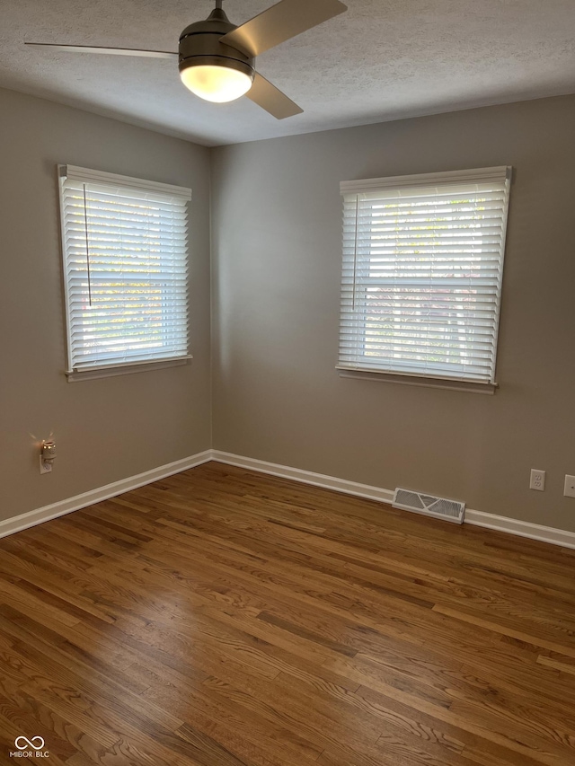 empty room with a wealth of natural light, dark hardwood / wood-style flooring, and a textured ceiling