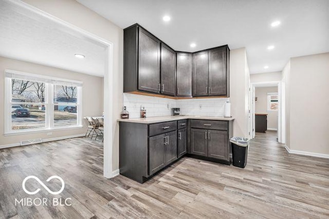 kitchen featuring light wood finished floors, baseboards, light countertops, dark brown cabinets, and backsplash