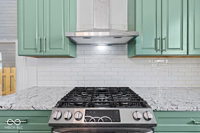 kitchen with backsplash, light stone countertops, stainless steel range oven, wall chimney exhaust hood, and green cabinetry