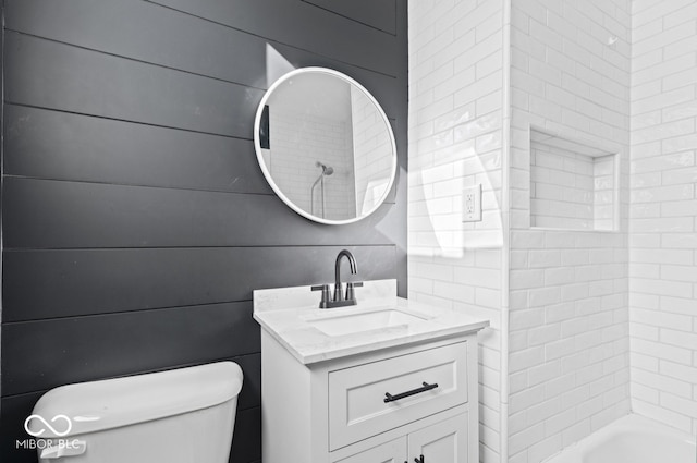 full bathroom featuring vanity, toilet, wood walls, and tiled shower / bath