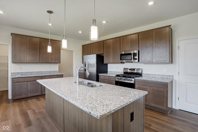 kitchen featuring dark hardwood / wood-style floors, hanging light fixtures, sink, light stone countertops, and appliances with stainless steel finishes