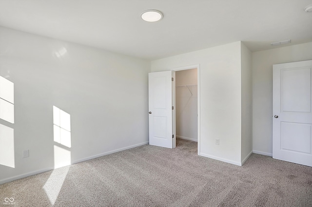 unfurnished bedroom featuring a walk in closet, a closet, and light colored carpet