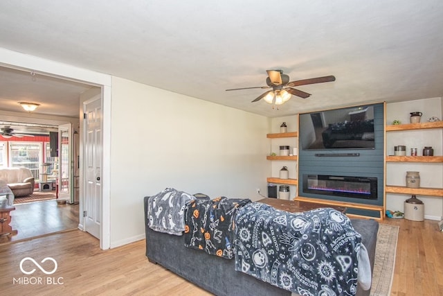 living room with light hardwood / wood-style floors, a large fireplace, and ceiling fan