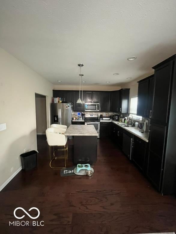 kitchen featuring sink, stainless steel appliances, dark hardwood / wood-style floors, decorative light fixtures, and a kitchen island