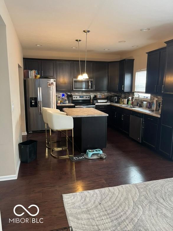 kitchen featuring a kitchen bar, stainless steel appliances, sink, pendant lighting, and a kitchen island