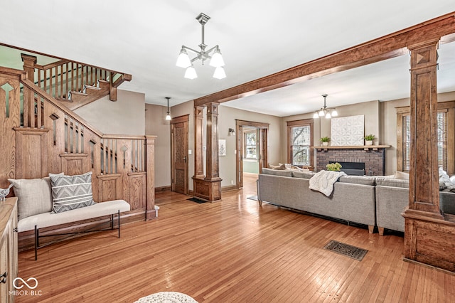 living room featuring a brick fireplace, light hardwood / wood-style floors, a chandelier, and decorative columns