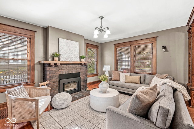 living room featuring a brick fireplace, a healthy amount of sunlight, an inviting chandelier, and light wood-type flooring