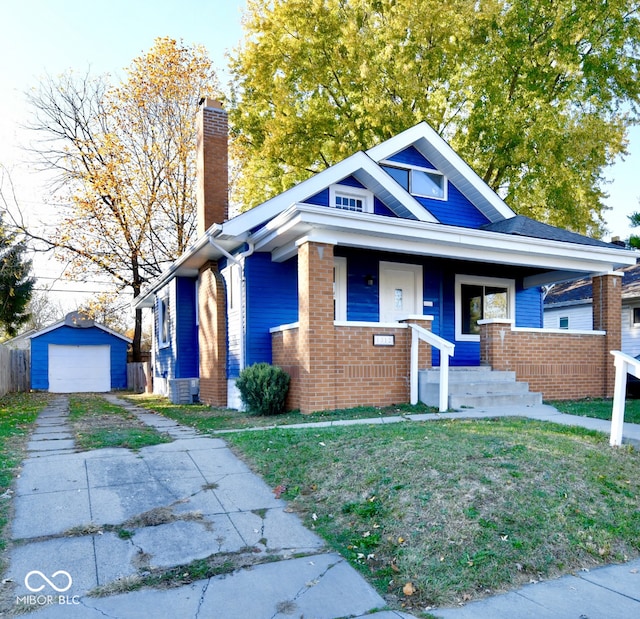 bungalow with a garage, covered porch, a front yard, an outbuilding, and central AC unit