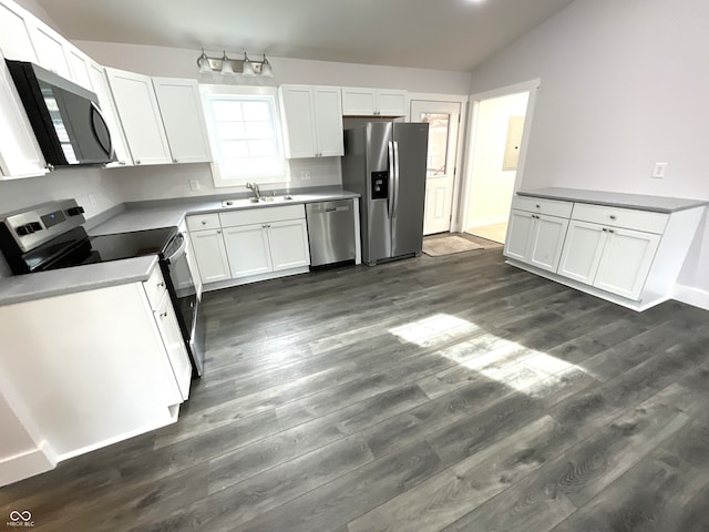 kitchen with vaulted ceiling, appliances with stainless steel finishes, sink, white cabinets, and dark wood-type flooring