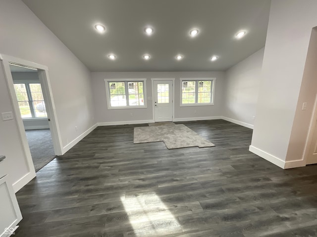 unfurnished living room featuring vaulted ceiling, dark hardwood / wood-style floors, and a wealth of natural light