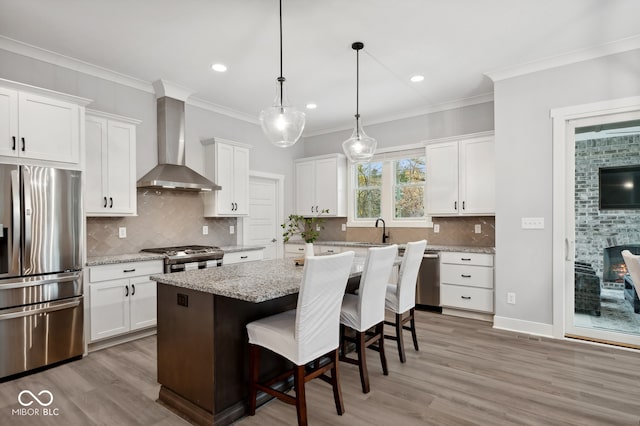 kitchen with a center island, stainless steel appliances, white cabinetry, wall chimney exhaust hood, and light hardwood / wood-style flooring