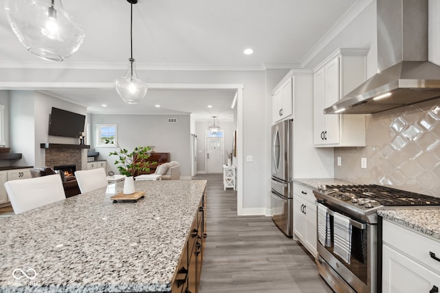 kitchen with white cabinetry, appliances with stainless steel finishes, light stone countertops, wall chimney exhaust hood, and wood-type flooring