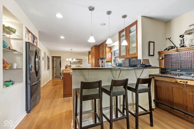 kitchen featuring light hardwood / wood-style floors, kitchen peninsula, a kitchen bar, an inviting chandelier, and black refrigerator