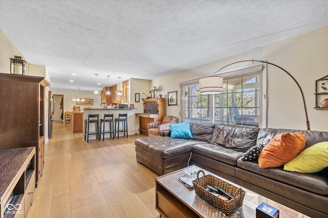 living room with light hardwood / wood-style floors, a textured ceiling, and an inviting chandelier