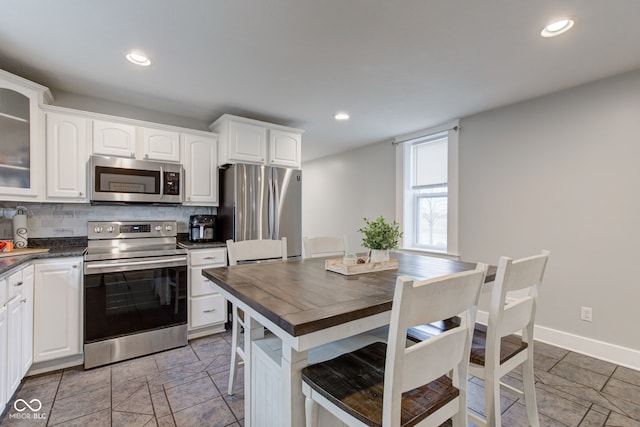 kitchen featuring tasteful backsplash, appliances with stainless steel finishes, a kitchen breakfast bar, white cabinets, and a center island