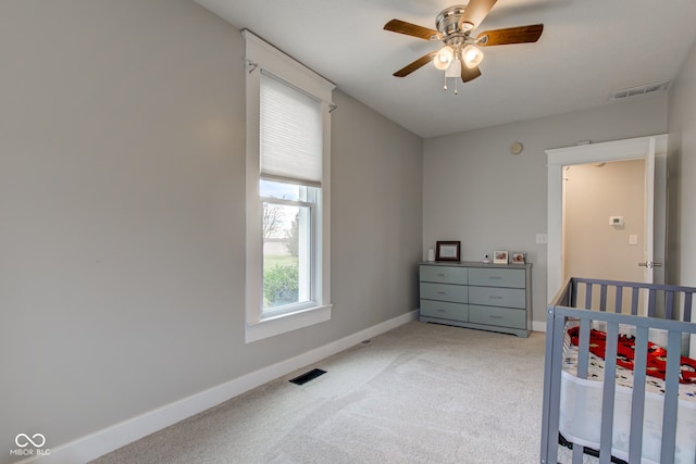 carpeted bedroom featuring a nursery area and ceiling fan