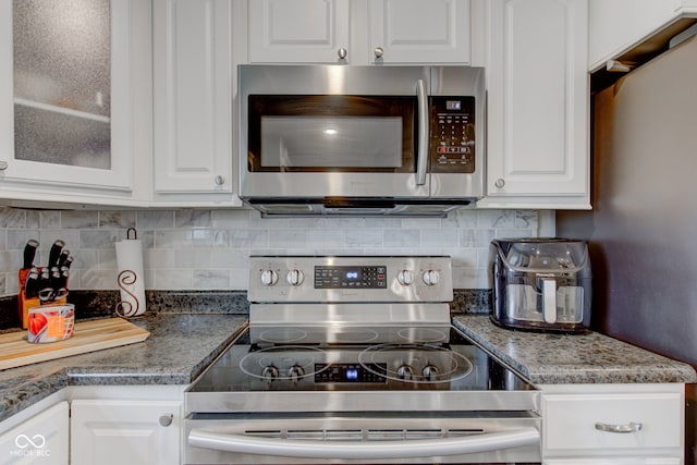 kitchen with white cabinets, appliances with stainless steel finishes, dark stone countertops, and backsplash