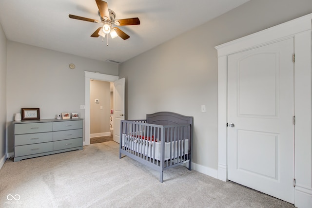 carpeted bedroom featuring ceiling fan and a crib