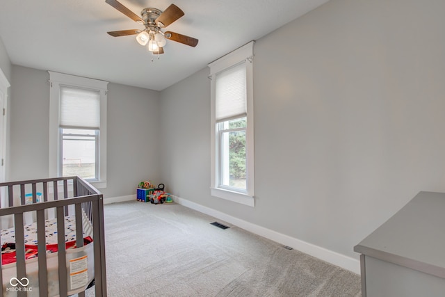 carpeted bedroom featuring a nursery area and ceiling fan