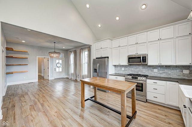 kitchen featuring white cabinets, stainless steel appliances, hanging light fixtures, and light hardwood / wood-style floors