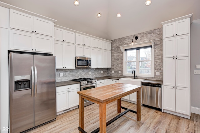 kitchen with white cabinetry, sink, stainless steel appliances, backsplash, and light wood-type flooring