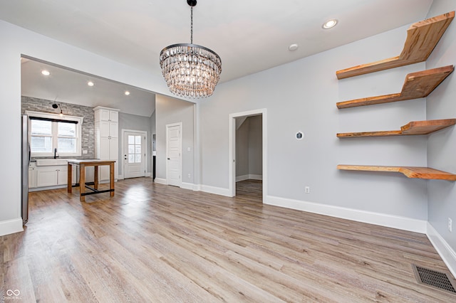 unfurnished living room with a chandelier, sink, and light hardwood / wood-style floors