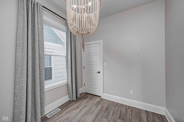 unfurnished room featuring plenty of natural light, light hardwood / wood-style flooring, and an inviting chandelier