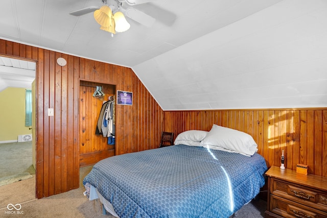 carpeted bedroom with wooden walls, vaulted ceiling, and ceiling fan