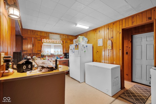 kitchen featuring kitchen peninsula, wood walls, fridge, and white fridge