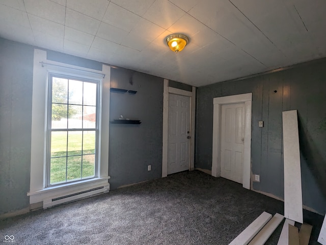 carpeted empty room with baseboard heating, wooden walls, and plenty of natural light