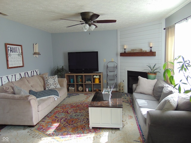 living room featuring ceiling fan, a textured ceiling, and a large fireplace