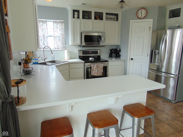 kitchen featuring stainless steel appliances, kitchen peninsula, a breakfast bar area, tasteful backsplash, and sink