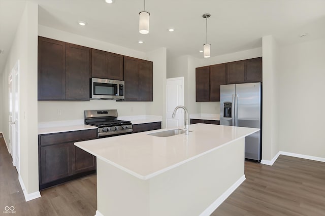 kitchen featuring stainless steel appliances, light hardwood / wood-style floors, a center island with sink, sink, and decorative light fixtures