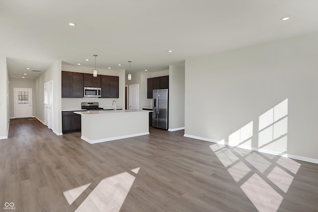 kitchen featuring a kitchen island with sink, appliances with stainless steel finishes, hardwood / wood-style flooring, and decorative light fixtures