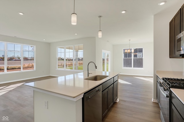 kitchen featuring stainless steel appliances, sink, decorative light fixtures, a kitchen island with sink, and light wood-type flooring