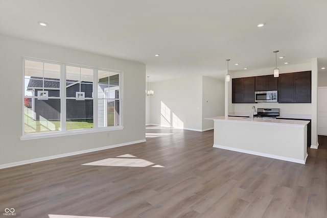 kitchen featuring light hardwood / wood-style floors, a center island with sink, appliances with stainless steel finishes, hanging light fixtures, and dark brown cabinets