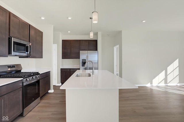 kitchen with light hardwood / wood-style floors, hanging light fixtures, sink, a kitchen island with sink, and appliances with stainless steel finishes