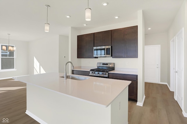 kitchen with sink, a kitchen island with sink, appliances with stainless steel finishes, and decorative light fixtures