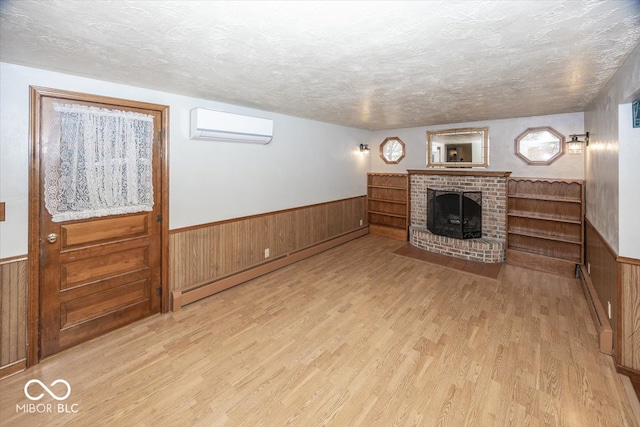 unfurnished living room featuring an AC wall unit, light wood-type flooring, a textured ceiling, and a fireplace