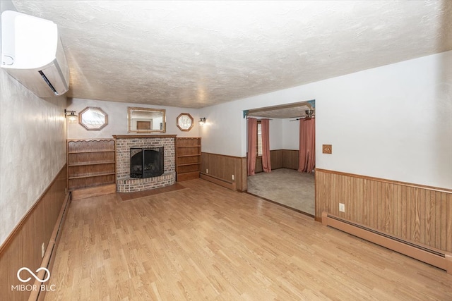 unfurnished living room featuring a wall unit AC, light hardwood / wood-style floors, a baseboard radiator, and a brick fireplace