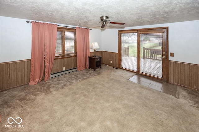 unfurnished living room featuring a baseboard radiator, wood walls, a textured ceiling, carpet, and ceiling fan